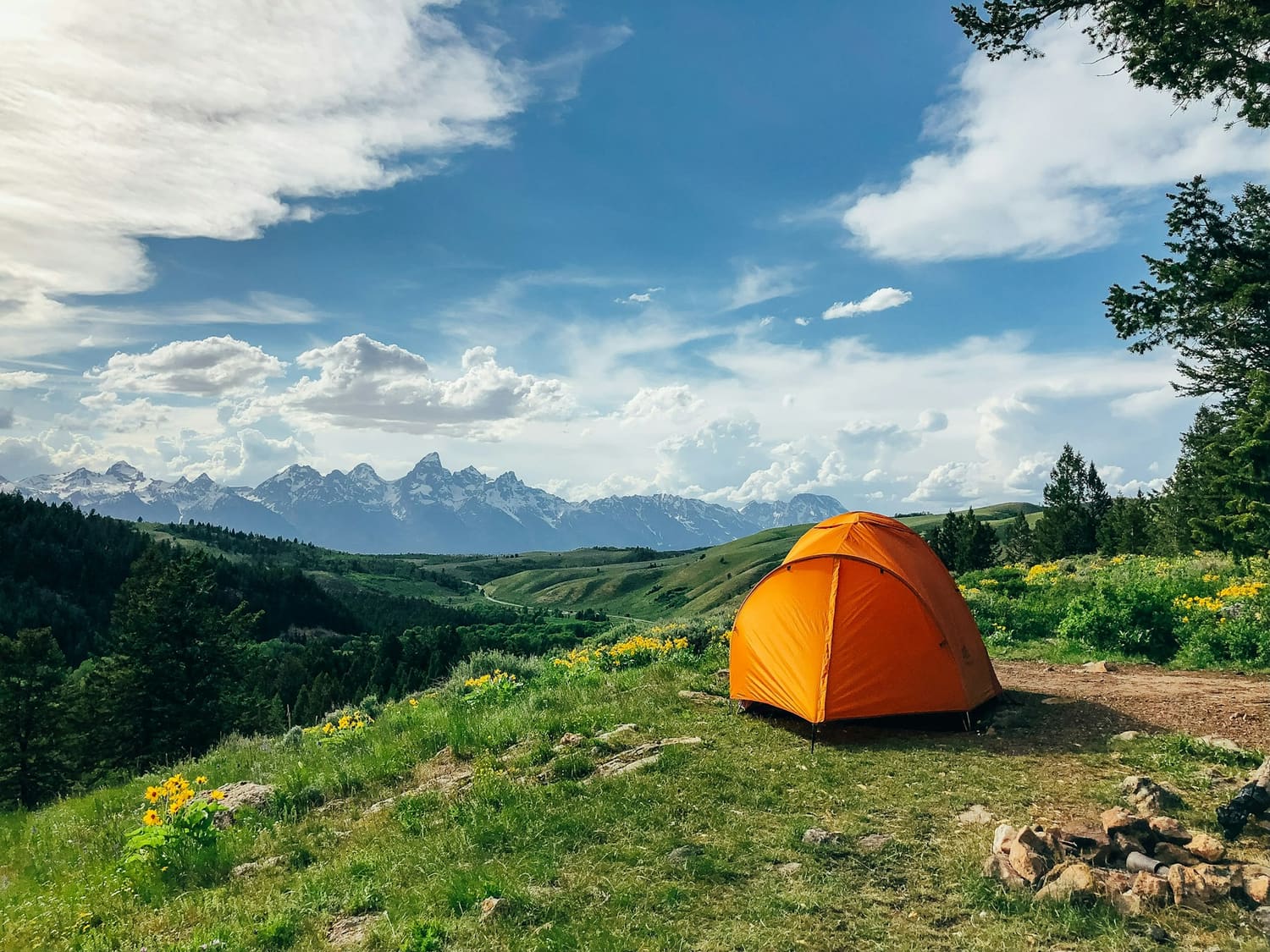 Orange tent pitched on a green hillside with mountains